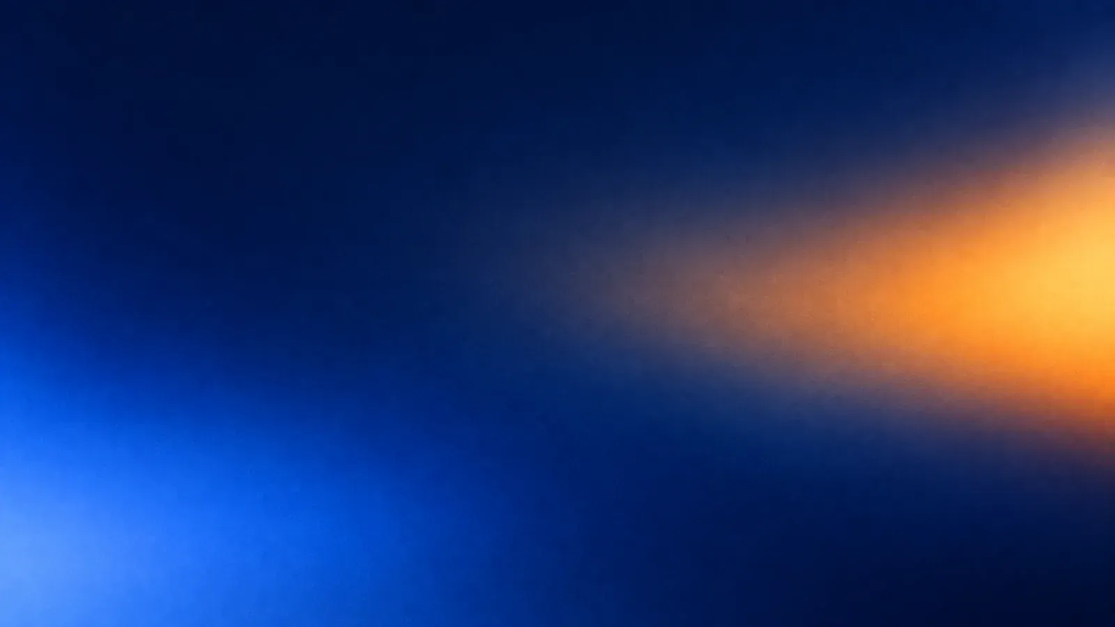 A soft blur of light on a dark blue field: an amber glow on the right and a blue glow in the lower left.