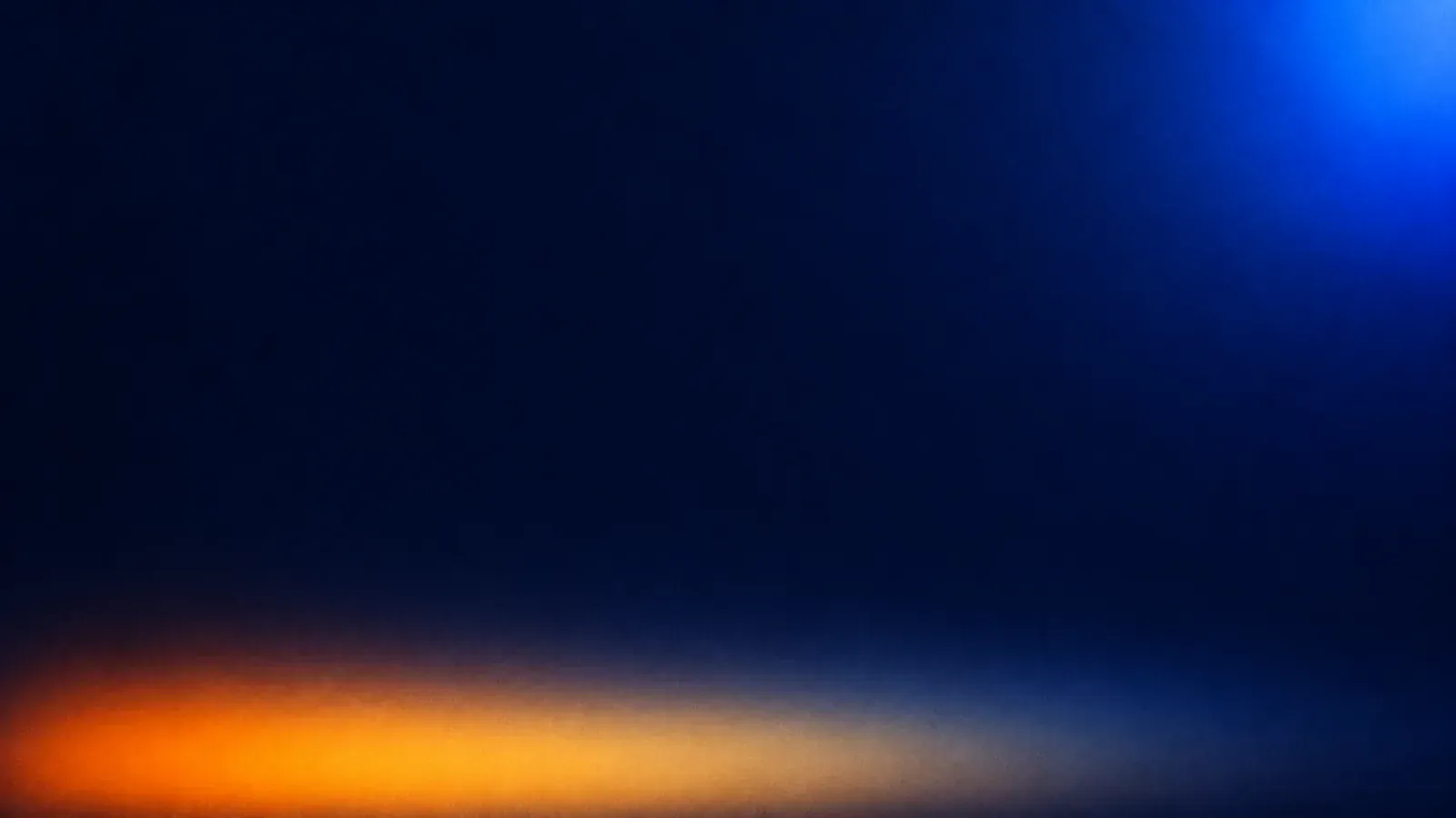 A soft blur of light on a near-black field: a low band of amber along the bottom and a blue glow in the upper right.